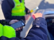 dwóch policjantów stojących przy samochodzie osobowym, jeden z nich trzyma w dłoni telefon komórkowy